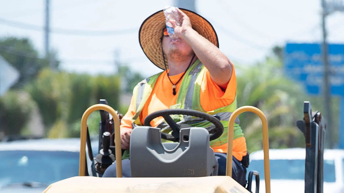 Tim Smith, of Roads Inc., tries to stay hydrated as he operates a roller in the blazing hot sun while working along Gulf Breeze Parkway in Santa Rosa County, Florida, on Friday, Aug. 4, 2023.