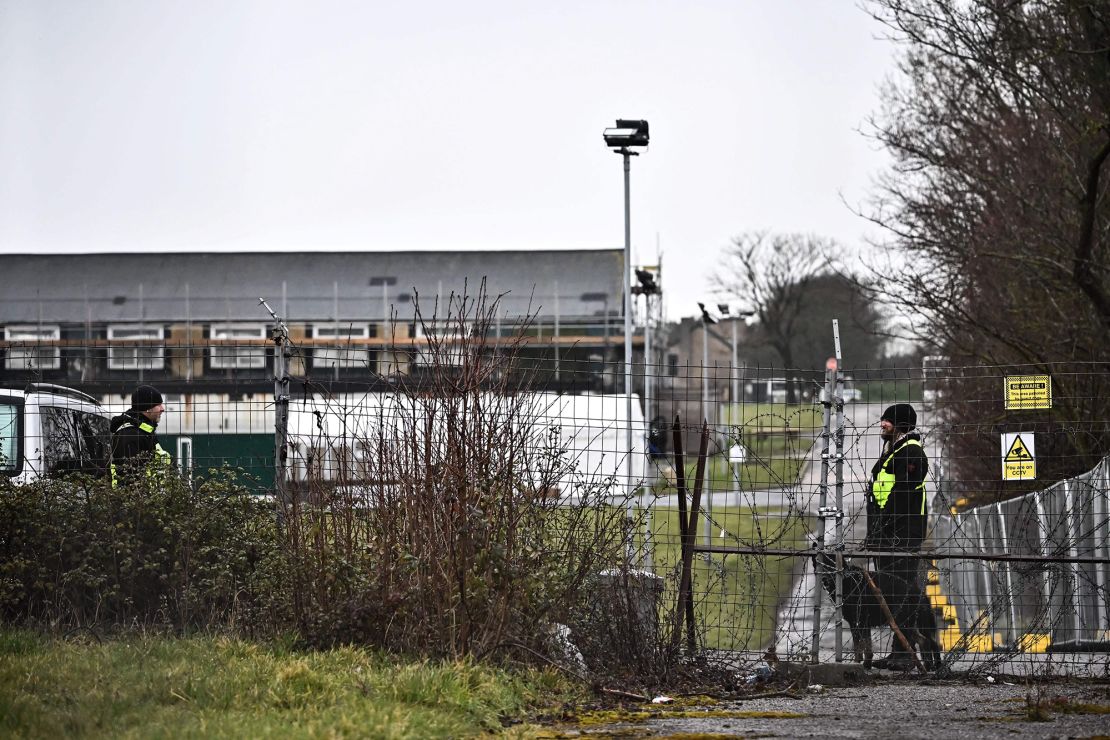 A guard patrols with a dog behind the fences surrounding Manston short-term holding centre for migrants, near Ramsgate in southeast England, on March 9, 2023 . - The Conservative government intends to outlaw asylum claims by all illegal arrivals and transfer them elsewhere, such as Rwanda, in a bid to stop thousands of migrants from crossing the Channel on small boats. But rights groups and the United Nations said the legislation would make Britain itself an international outlaw under European and UN conventions on asylum. (Photo by Ben Stansall / AFP) (Photo by BEN STANSALL/AFP via Getty Images)