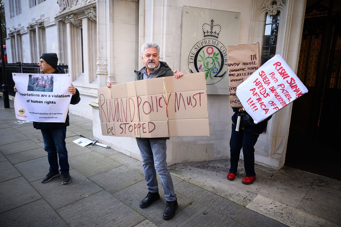 LONDON, ENGLAND - NOVEMBER 15: Protestors hold placards as they wait for the verdict on whether the UK Government can send refugee migrants to Rwanda, as they gather outside The Supreme Court on November 15, 2023 in London, England. The UK's Court of Appeal declared the government's deportation scheme to Rwanda unlawful in June 2023, citing concerns about the country's safety.  (Photo by Leon Neal/Getty Images)