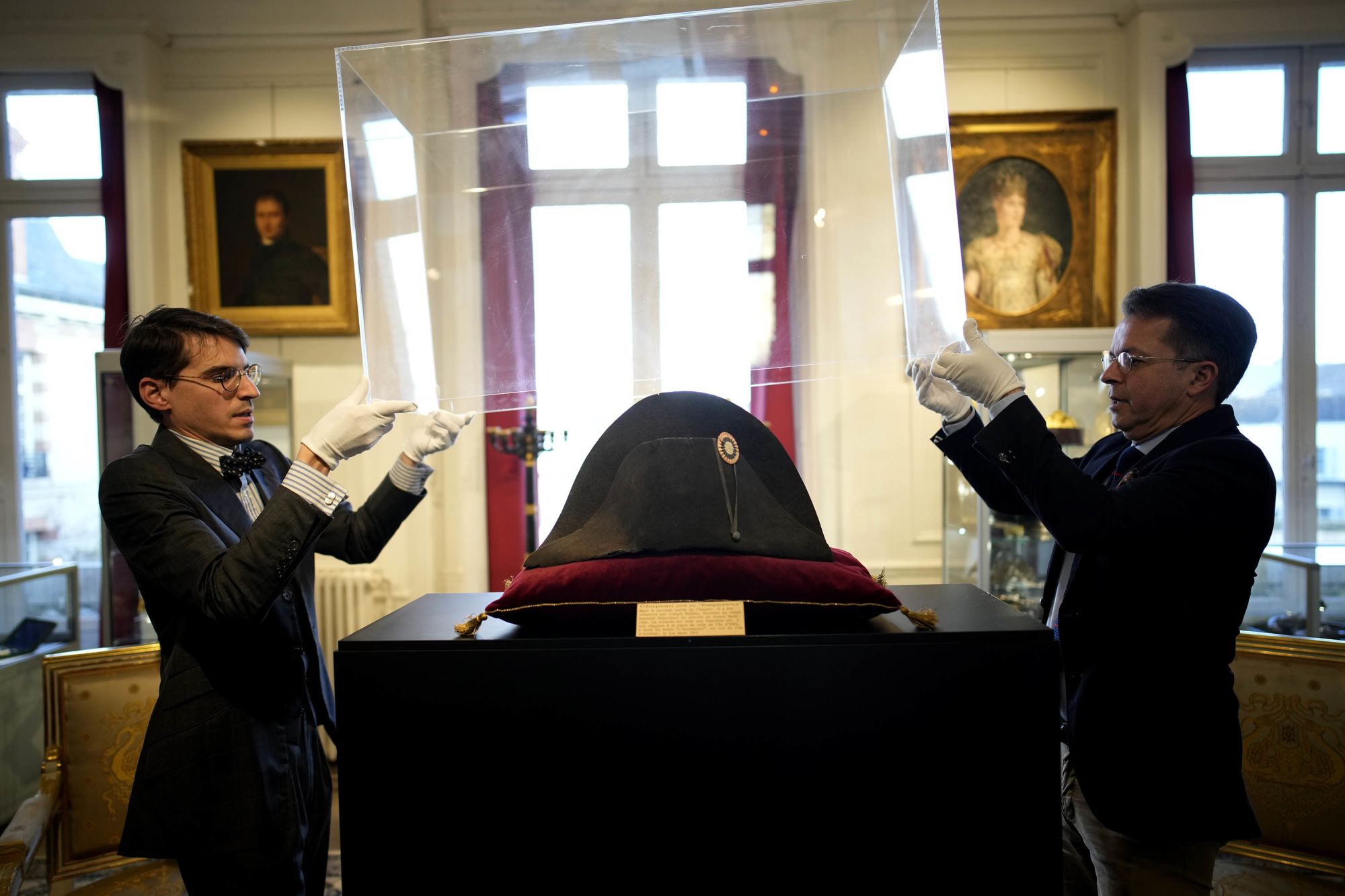 Raphael Pitchal, left, and Jean Christophe Chataignier of Osenat's auction house remove the protection of one of the signature broad, black hats that Napoléon wore when he ruled 19th century France and waged war in Europe at Osenat's auction house in Fontainebleau, south of Paris, Friday, Nov. 17, 2023. The hat is tipped to fetch more than half a million euros (dollars) at the auction Sunday of Napoleonic memorabilia patiently collected by a French industrialist. (AP Photo/Christophe Ena)