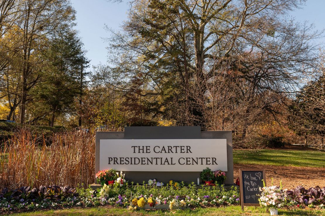 Flowers are laid at the base of a sign at the entrance of the Carter Presidential Center in Atlanta on November 27, 2023.