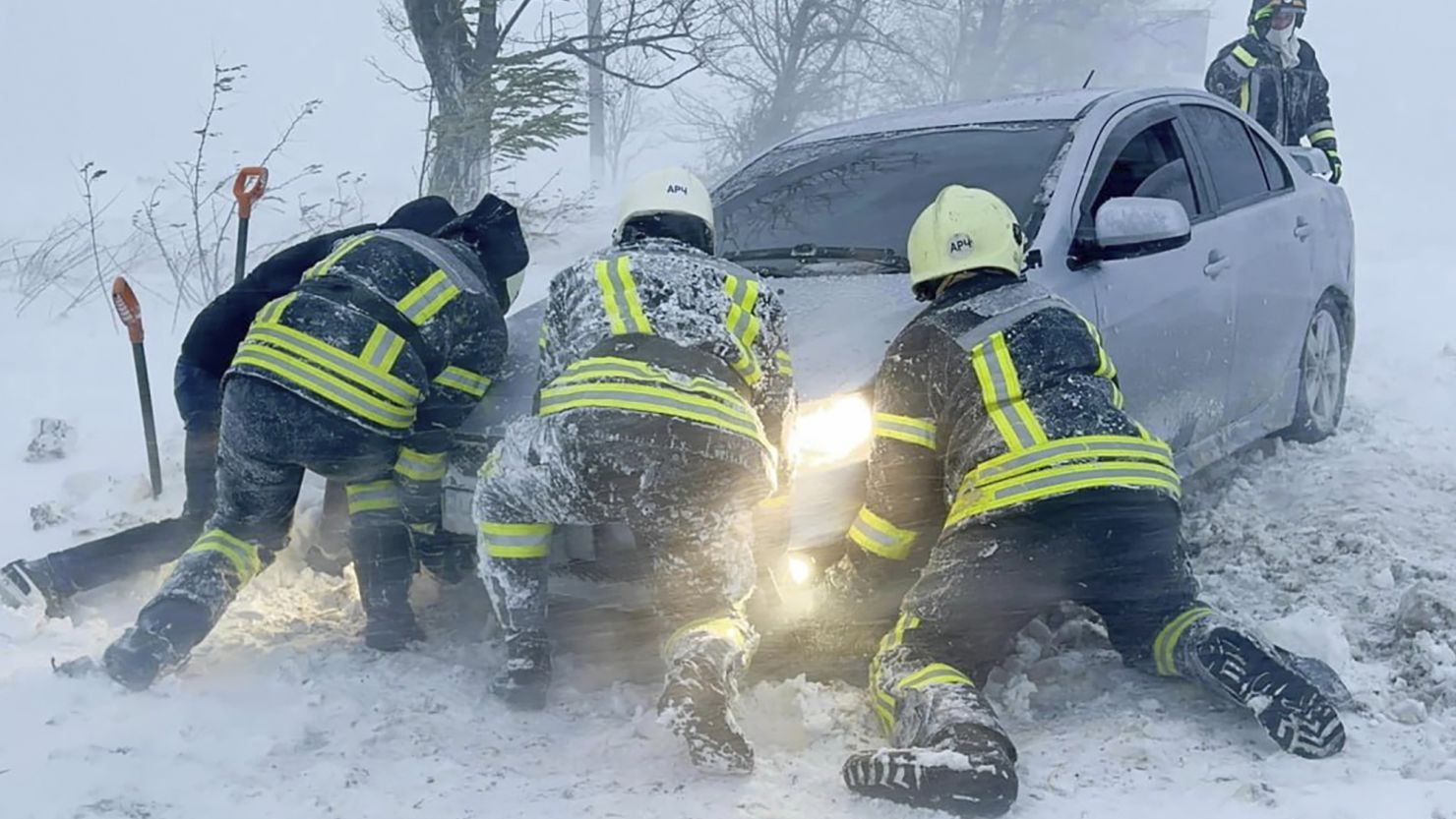 Emergency workers try to push a car trapped in snow on the Odesa region highway in Ukraine, November 27, 2023.