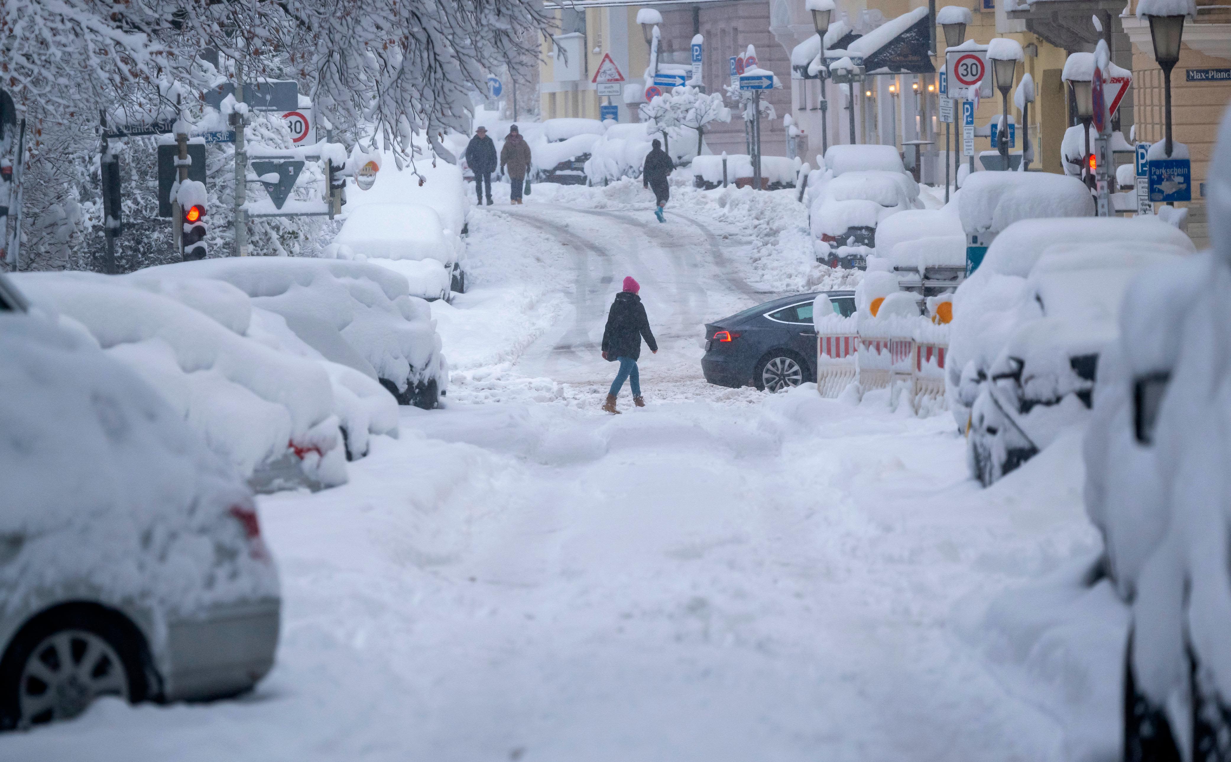 02 December 2023, Bavaria, Munich: Passers-by walk along a snow-covered road. Snow and ice have caused chaos on the roads and on the railroads in southern Bavaria.