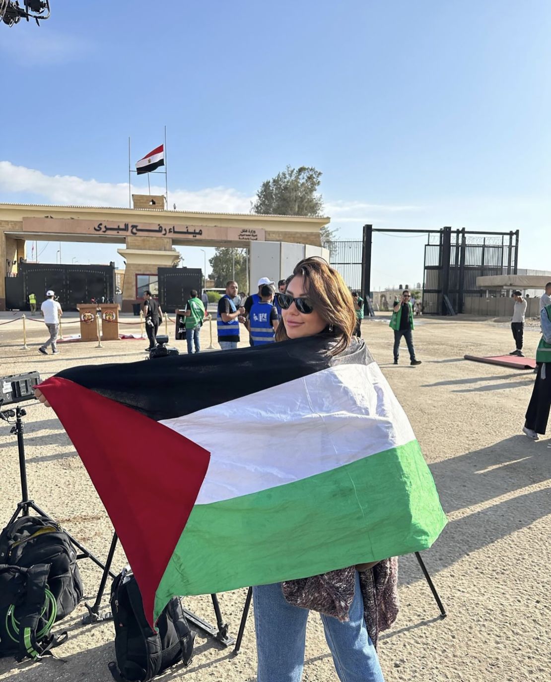 El Helbawi stands at the Rafah border crossing between Gaza and Egypt with a Palestinian flag draped across her back.