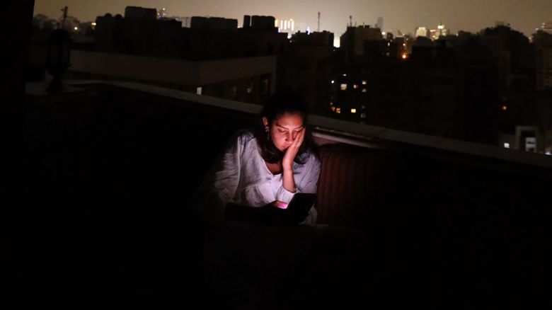 Mirna El Helbawi sits on a rooftop in Cairo, Egypt, using her phone to coordinate the distribution of virtual SIM cards in Gaza.