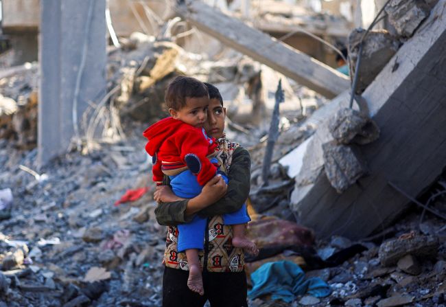 A Palestinian boy carrying a baby stands at a site of Israeli strikes in Rafah, southern Gaza, on December 4.