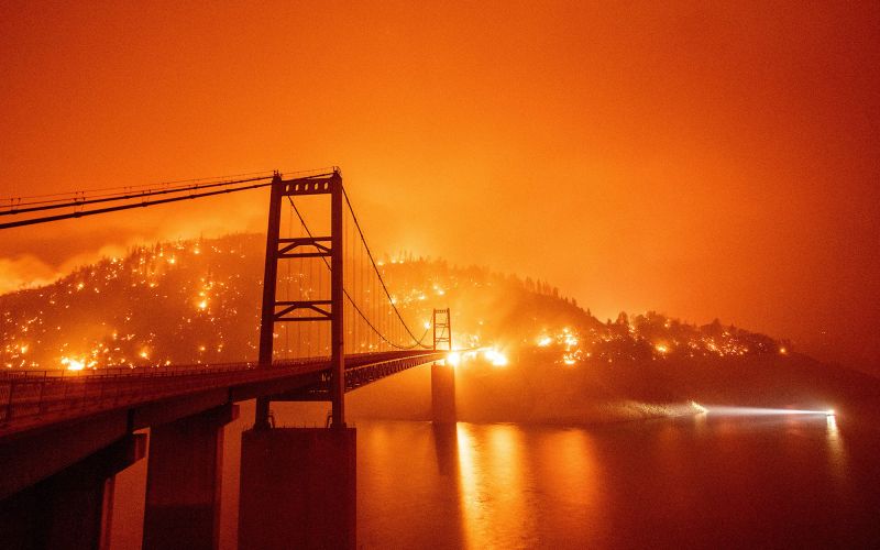 A boat motors by as the Bidwell Bar Bridge is surrounded by fire in Lake Oroville during the Bear fire in Oroville, California on September 9, 2020. - Dangerous dry winds whipped up California's record-breaking wildfires and ignited new blazes Tuesday, as hundreds were evacuated by helicopter and tens of thousands were plunged into darkness by power outages across the western United States. (Photo by JOSH EDELSON / AFP) (Photo by JOSH EDELSON/AFP via Getty Images)