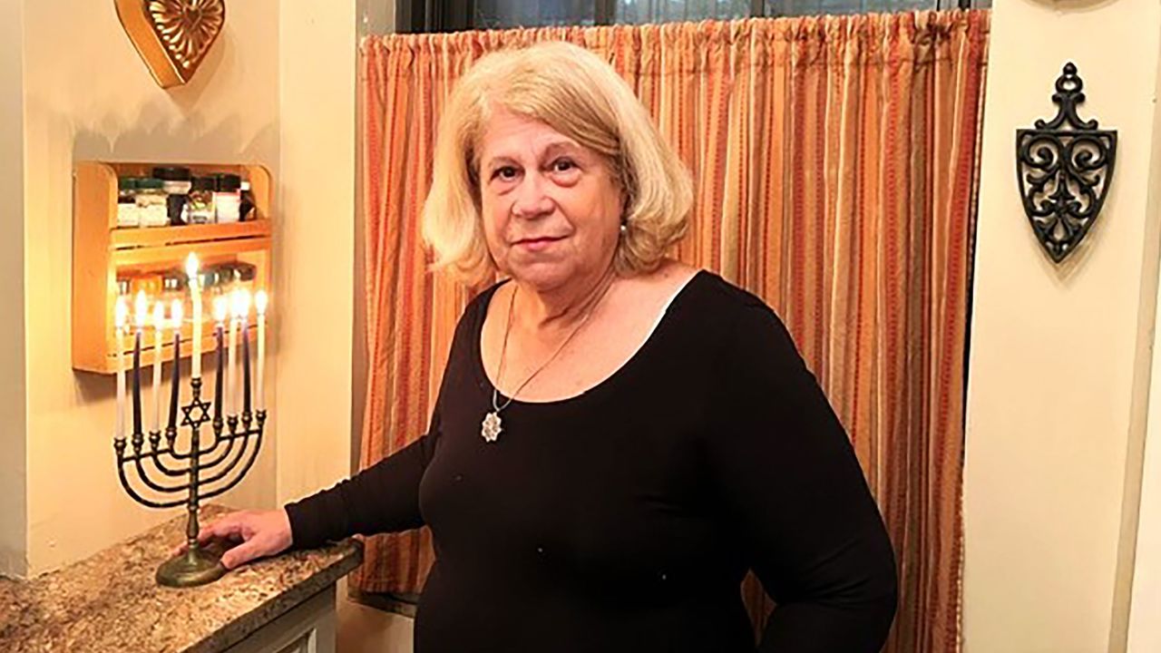 Jean Joachim stands with her menorah near a closed window at her home in New York.