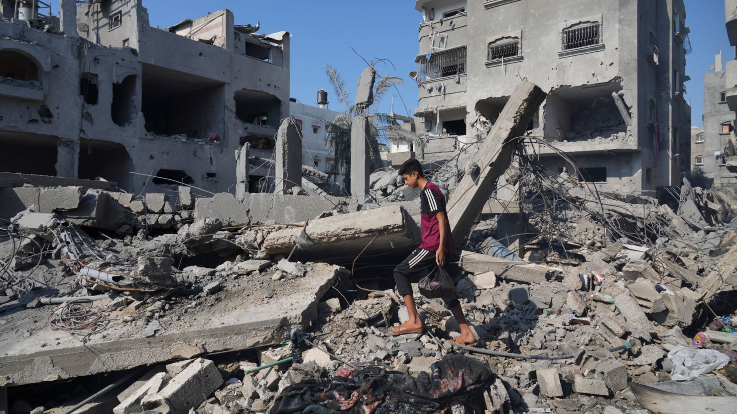 Palestinians stand by the building destroyed in an Israeli airstrike in Deir al-Balah, south of the Gaza Strip, Saturday, Oct. 14, 2023. (AP Photo/Hatem Moussa)