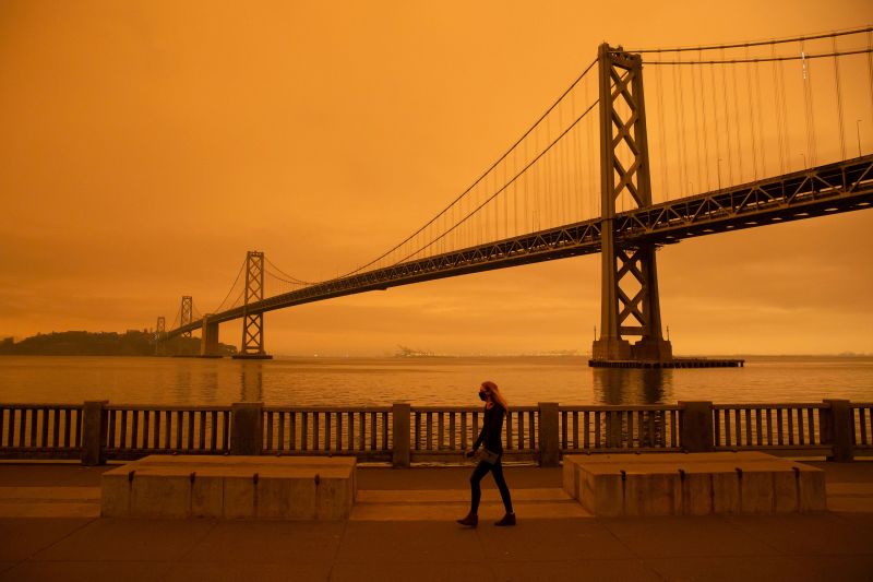 TOPSHOT - A woman walks along The Embarcadero under an orange smoke-filled sky in San Francisco, California on September 9, 2020. - More than 300,000 acres are burning across the northwestern state including 35 major wildfires, with at least five towns
