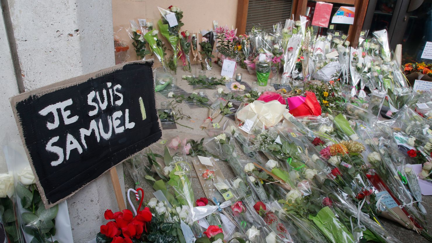 A poster reading "I am Samuel" and flowers lay outside the school where slain history teacher Samuel Paty was working, Saturday, Oct. 17, 2020 in Conflans-Sainte-Honorine, northwest of Paris.