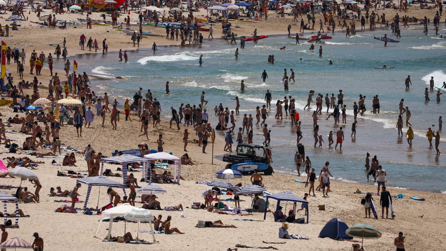 Beachgoers sit and stand on the sand as others swim on a hot summer day at Sydney's Bondi Beach on December 9, 2023.
