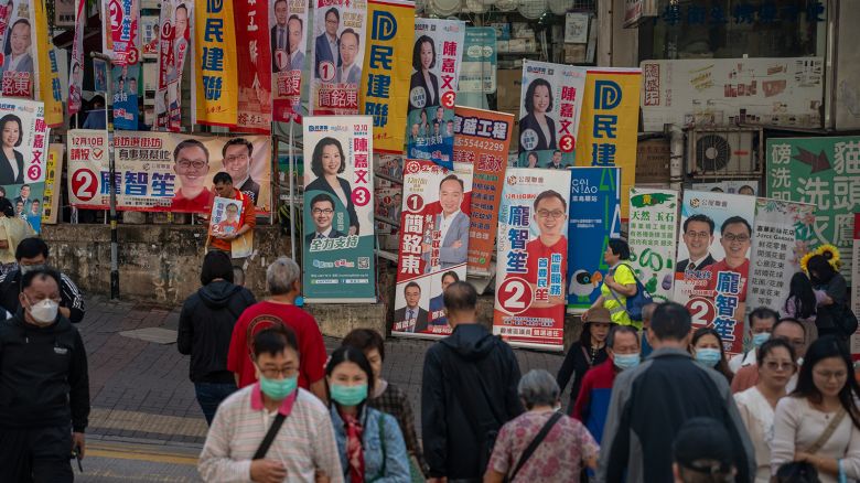 People are crossing the road in front of banners for a candidate of the 2023 District Council Election in Hong Kong, China, on December 10, 2023.