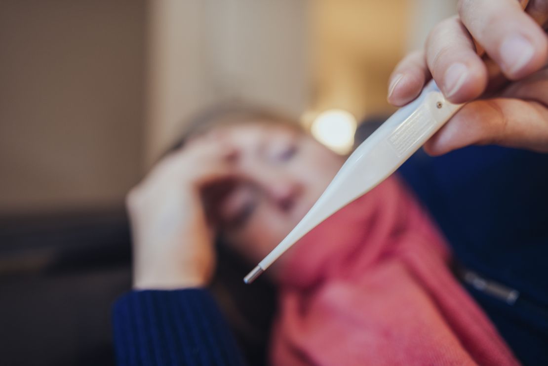 Ill woman looking at thermometer at home.