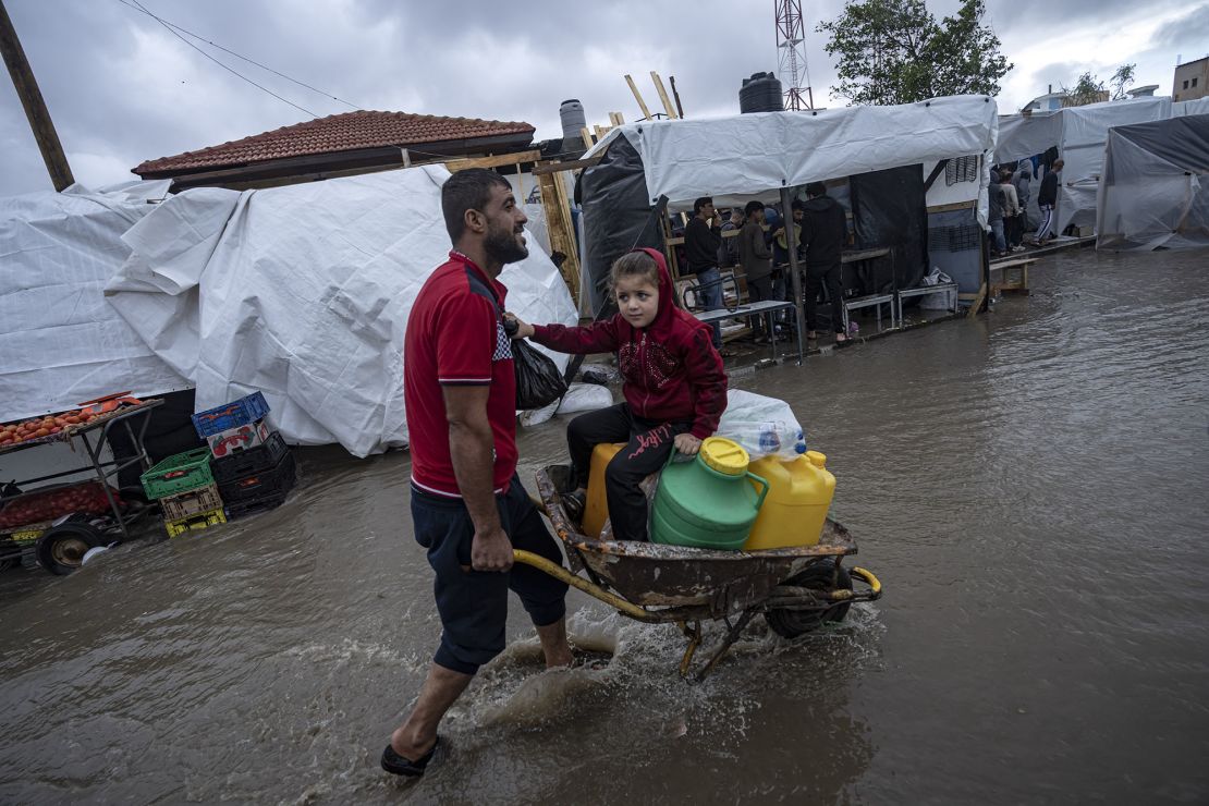 A man carries his daughter in a wheelbarrow through the flooded streets of a U.N. displacement camp after rainfall in the southern town of Khan Younis, Gaza Strip, Sunday, Nov. 19, 2023. Hundreds of thousands of Palestinians have fled their homes in northern Gaza as Israel moves ahead with a ground offensive against the ruling Hamas militant group. (AP Photo/Fatima Shbair)