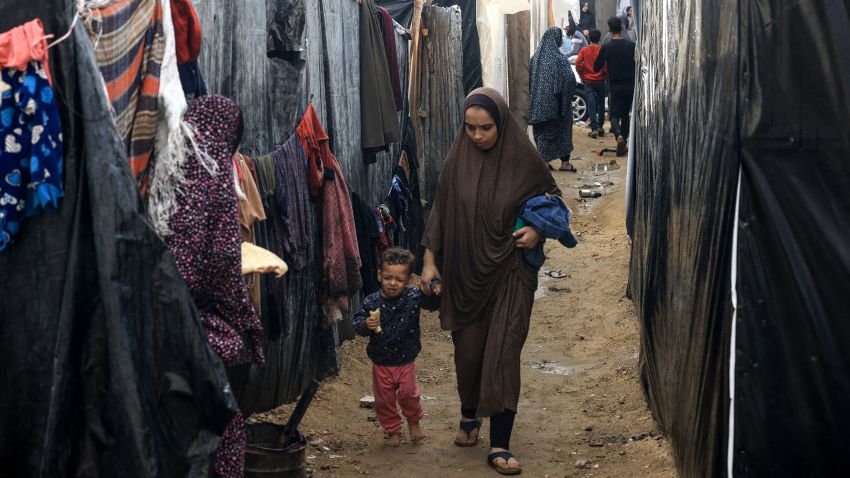A Palestinian woman and a child walk amidst the rain at camp for displaced people in Rafah, in the southern Gaza Strip, where most civilians have taken refuge as battles continue between Israel and the Palestinian militant group Hamas, on December 12, 2023. (Photo by MAHMUD HAMS / AFP) (Photo by MAHMUD HAMS/AFP via Getty Images)