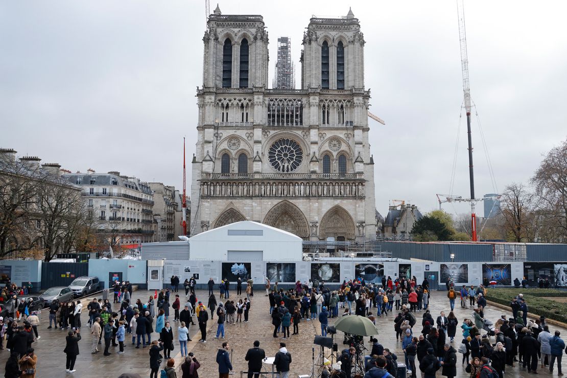 People stand in front of Notre-Dame de Paris Cathedral during the reconstruction work on the Ile de la Cite in Paris, on December 8, 2023, one year to the day before the cathedral, which was ravaged by fire in 2019, is due to reopen. (Photo by Ludovic MARIN / AFP) (Photo by LUDOVIC MARIN/AFP via Getty Images)