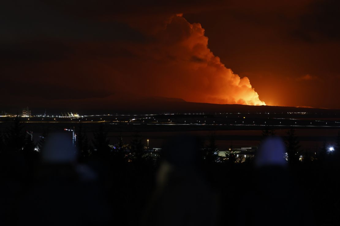 People watch as the night sky is illuminated caused by the eruption of a volcano on the Reykjanes peninsula of south-west Iceland seen from the capital city of Reykjavik, Monday Dec. 18, 2023. (AP Photo/Brynjar Gunnarsson)