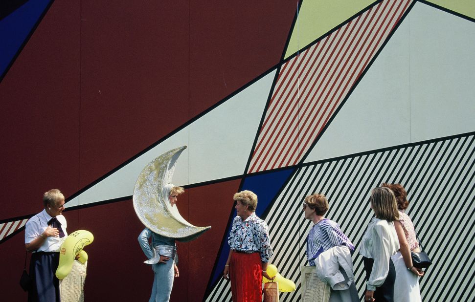 A celestial performer speaks with park-goers in front of Roy Lichtenstein's Luna Luna Pavilion — a venue within the park designed in the pop artist's signature style. © Estate of Roy Lichtenstein, 1987, all rights reserved.