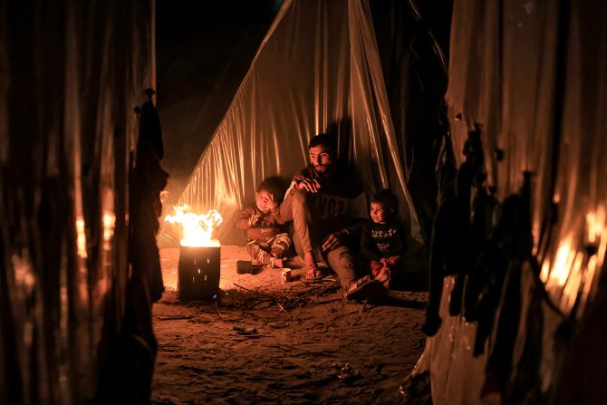 A man sits with children by a fire outside one of the tents housing displaced Palestinians, in Rafah, Gaza, on December 18.