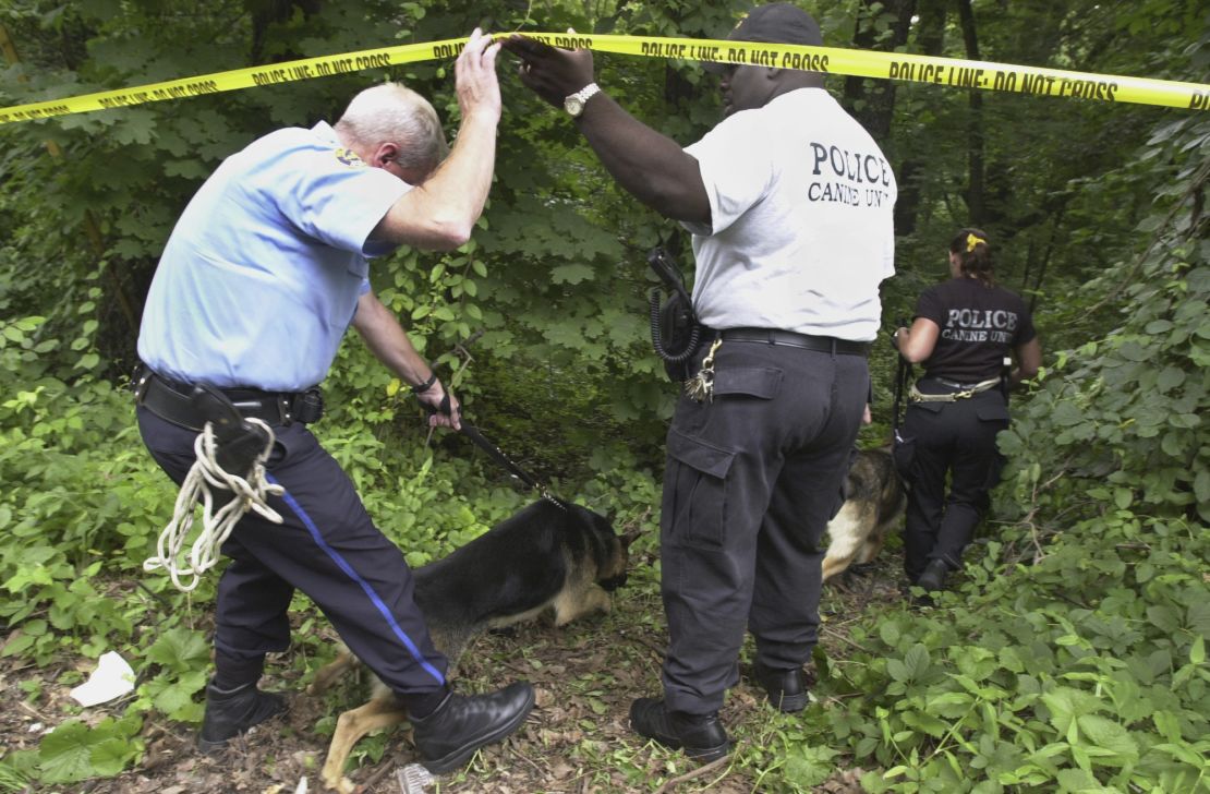 FILE - Philadelphia K-9 unit police walk into an area of Fairmount Park where the body of a woman, suspected to be that of fourth-year medical student Rebecca Park, was discovered, July 17, 2003, during an ongoing investigation of the scene the following day, July 18, in Philadelphia. Authorities say a man accused of slashing people with a large knife while riding a bicycle on a rail trail in Philadelphia is now a person of interest in the murder of Park that occurred among a series of high-profile sexual assaults two decades earlier. (AP Photo/Jacqueline Larma, File)