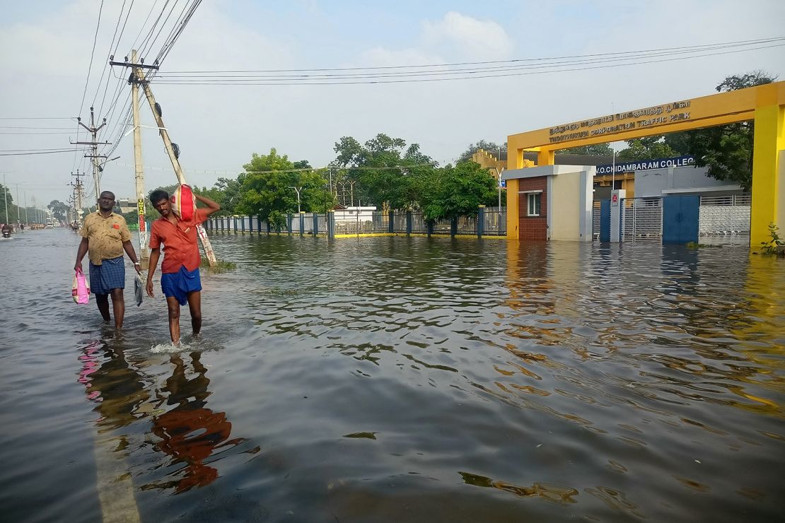 People carrying their belongings walk through a flooded street in Thoothukudi on December 20, 2023.