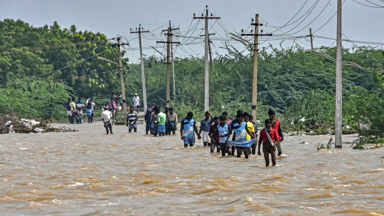 People wade through a flooded road after heavy rains in Thoothukudi on December 20, 2023.