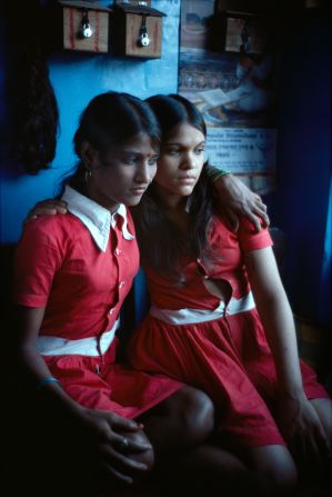 Two girls sit with their arms around each other.
