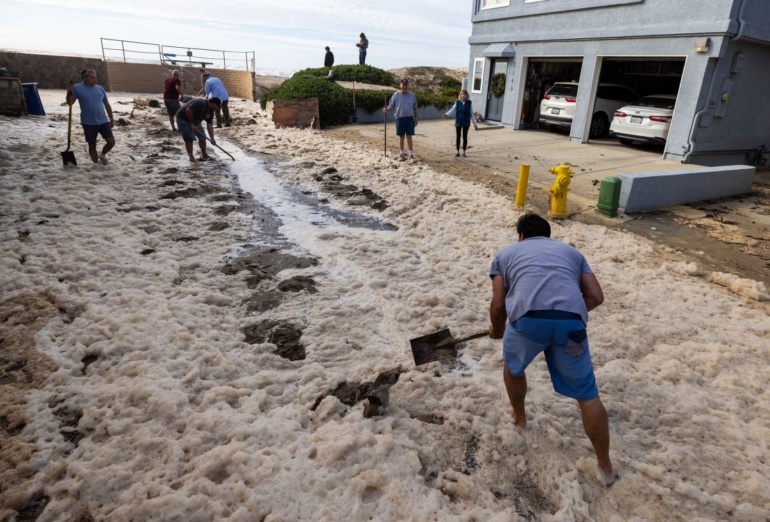 Ventura, CA - December 28: Pierpont neighbors help shovel sand on Bath Lane to help water drain after a seawall and sand berm was breached by high surf on Thursday, Dec. 28, 2023 in Ventura, CA. (Brian van der Brug / Los Angeles Times via Getty Images)