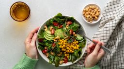 Anonymous female dining healthy vegan plant-based salad in bowl with avocado, cashew, micro-greens, pok choi, chickpeas, tomato, lettuce, cucumber, sesame. Flexitarian fatty acids and dietary fiber