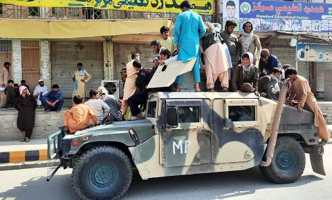 Taliban fighters and local residents sit over an Afghan National Army (ANA) humvee vehicle along the roadside in Laghman province on August 15.