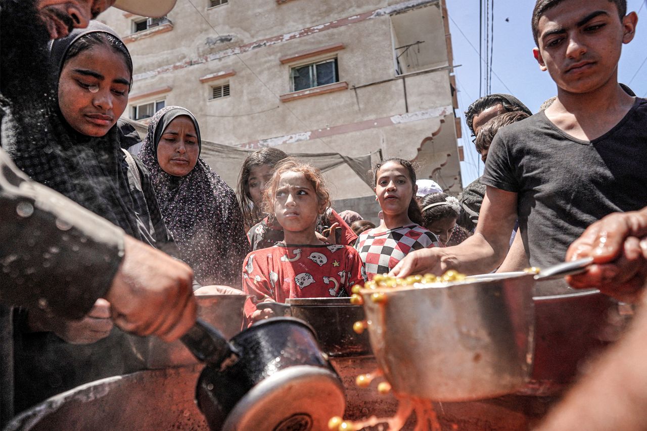 People are handed food portions from a large pot at a public kitchen in Deir al-Balah, central Gaza, on May 13.