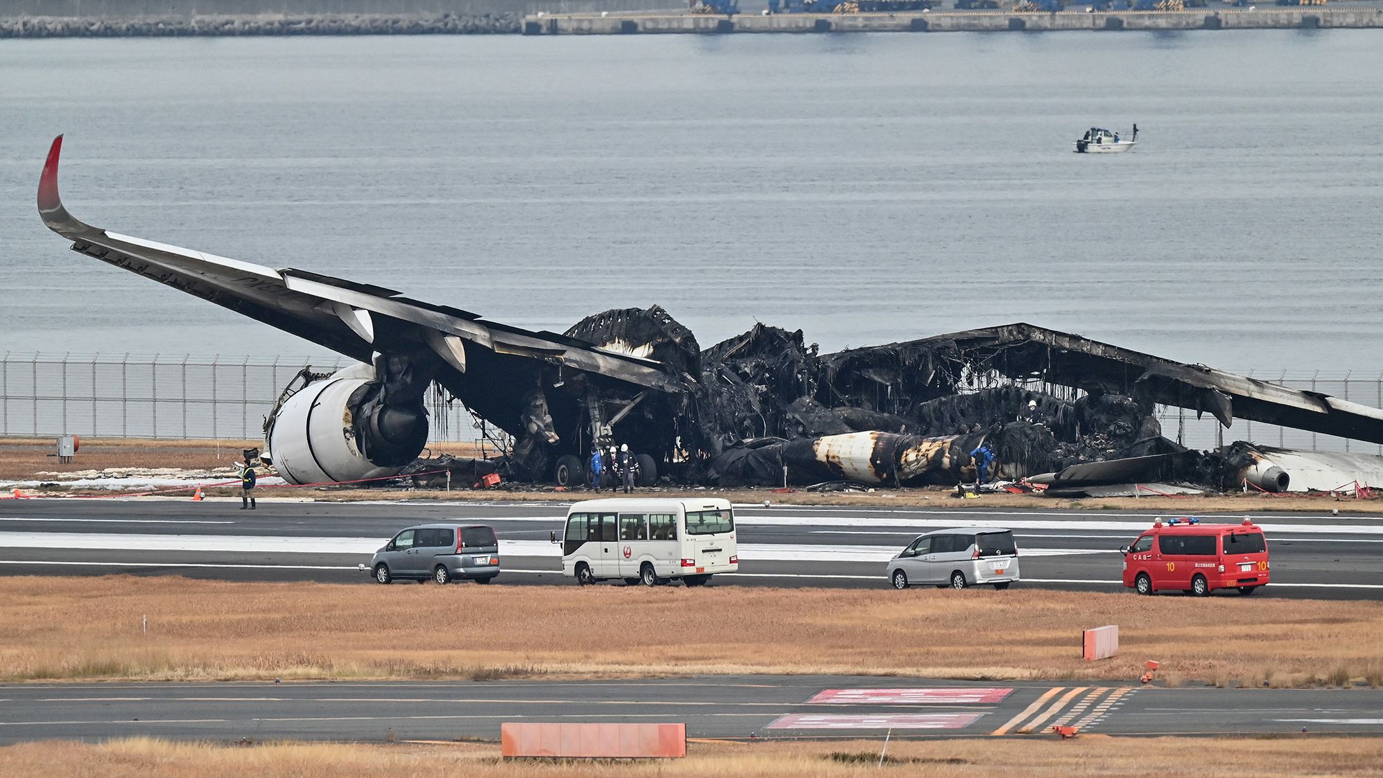 TOPSHOT - Officials look at the burnt wreckage of a Japan Airlines (JAL) passenger plane on the tarmac at Tokyo International Airport at Haneda in Tokyo on January 3, 2024, the morning after the JAL airliner hit a smaller coast guard plane on the ground. Five people aboard a Japan coast guard aircraft died on January 2 when it hit a Japan Airlines passenger plane on the ground in a fiery collision at Tokyo's Haneda airport. (Photo by Richard A. Brooks / AFP) (Photo by RICHARD A. BROOKS/AFP via Getty Images)