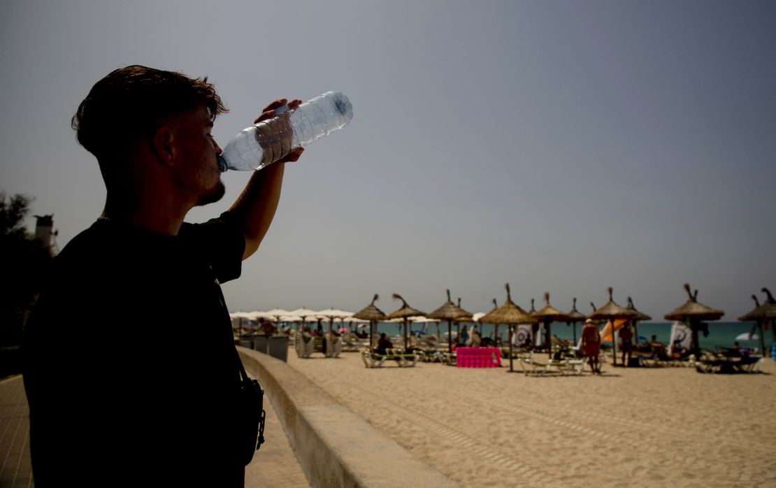 18 July 2023, Spain, Palma de Mallorca: Etienne from Biberach drinks water in hot temperatures on the beach of Arenal. For the north and east of the Spanish Mediterranean island of Mallorca, the national weather service Aemet announced maximum temperatures of at least 43 degrees. The peak of the third heat wave of the summer in Spain makes locals and tourists in the popular vacation destination sweat. Photo: Clara Margais/dpa (Photo by Clara Margais/picture alliance via Getty Images)