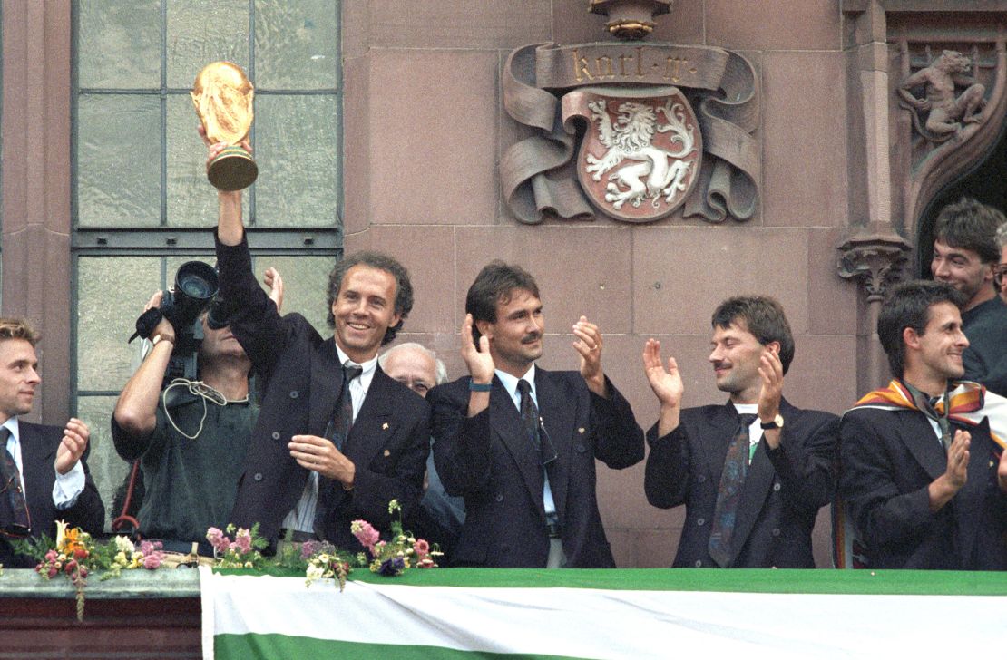 Team manager Franz Beckenbauer is holding up the World Cup trophy on the balcony of Frankfurt's town hall, the Roemer; Raimond Aumann, Guenther Hermann and Pierre Littbarski are standing next to him. (Photo by Kai-Uwe Wärner/picture alliance via Getty Images)