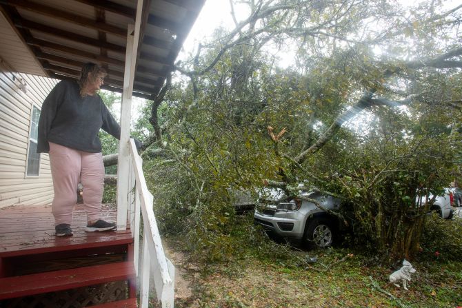 Linda Cox looks at her two vehicles that were damaged by a fallen tree in Myrtle Grove, Florida.