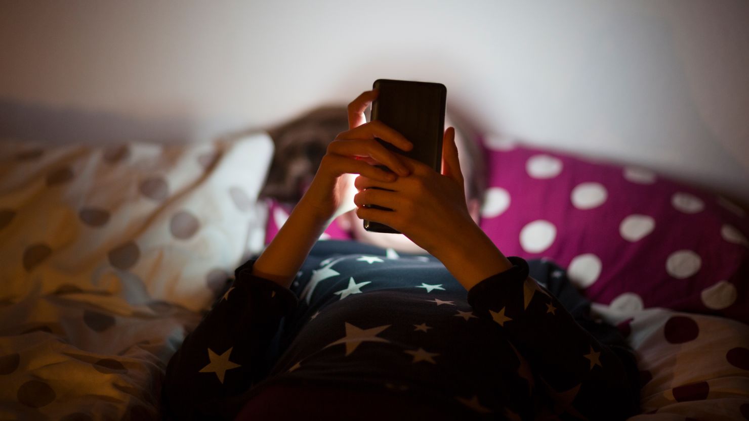 Girl lying on bed at night and using a mobile phone - stock photo