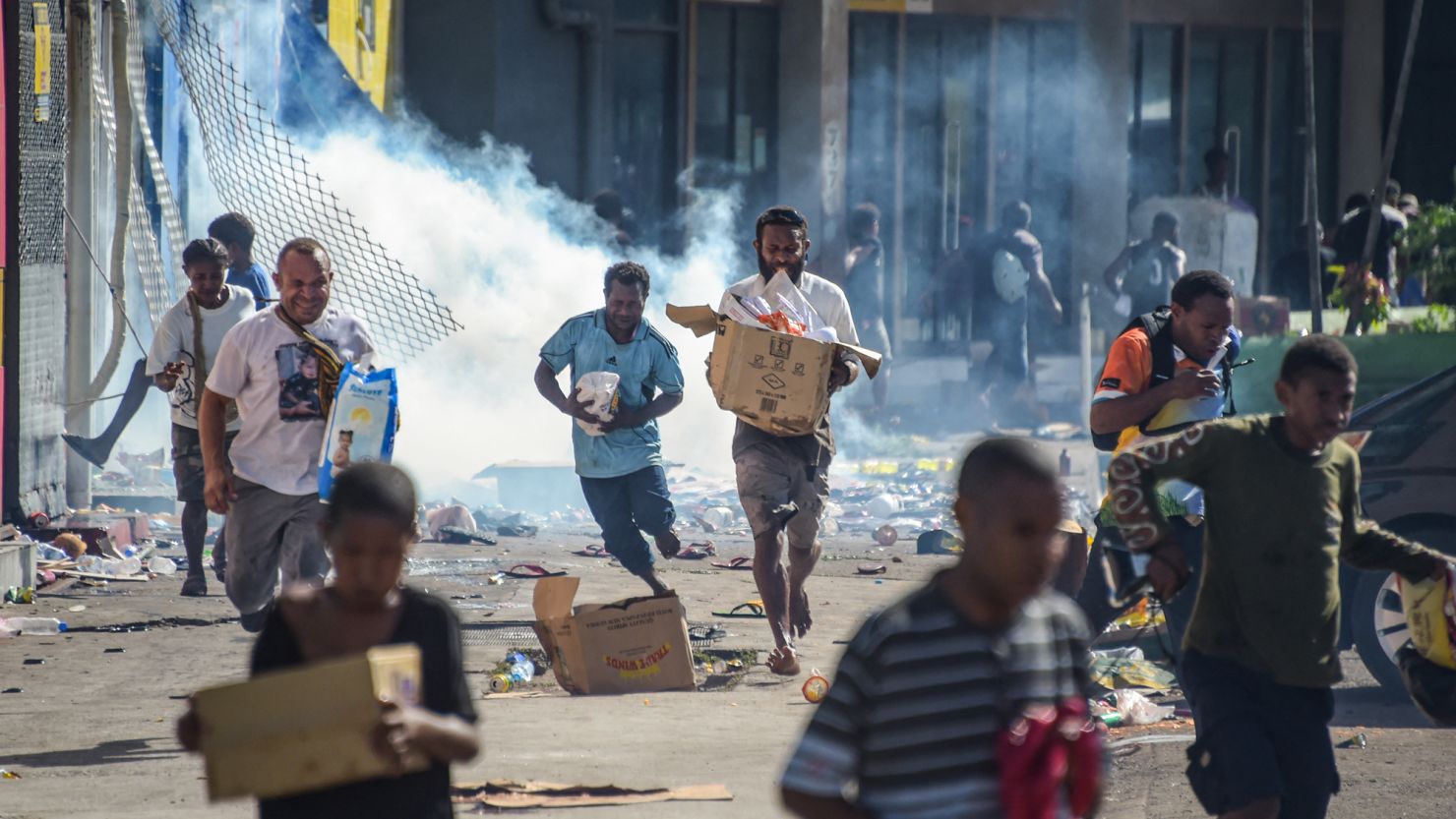 TOPSHOT - People run with merchandise as crowds leave shops with looted goods amid a state of unrest in Port Moresby on January 10, 2024. A festering pay dispute involving Papua New Guinea's security forces on January 10 sparked angry protests in the capital, where a crowd torched a police car outside the prime minister's office. By Wednesday afternoon pockets of unrest had spread through the capital Port Moresby, with video clips on social media showing crowds looting shops and stretched police scrambling to restore order. (Photo by Andrew KUTAN / AFP) (Photo by ANDREW KUTAN/AFP via Getty Images)