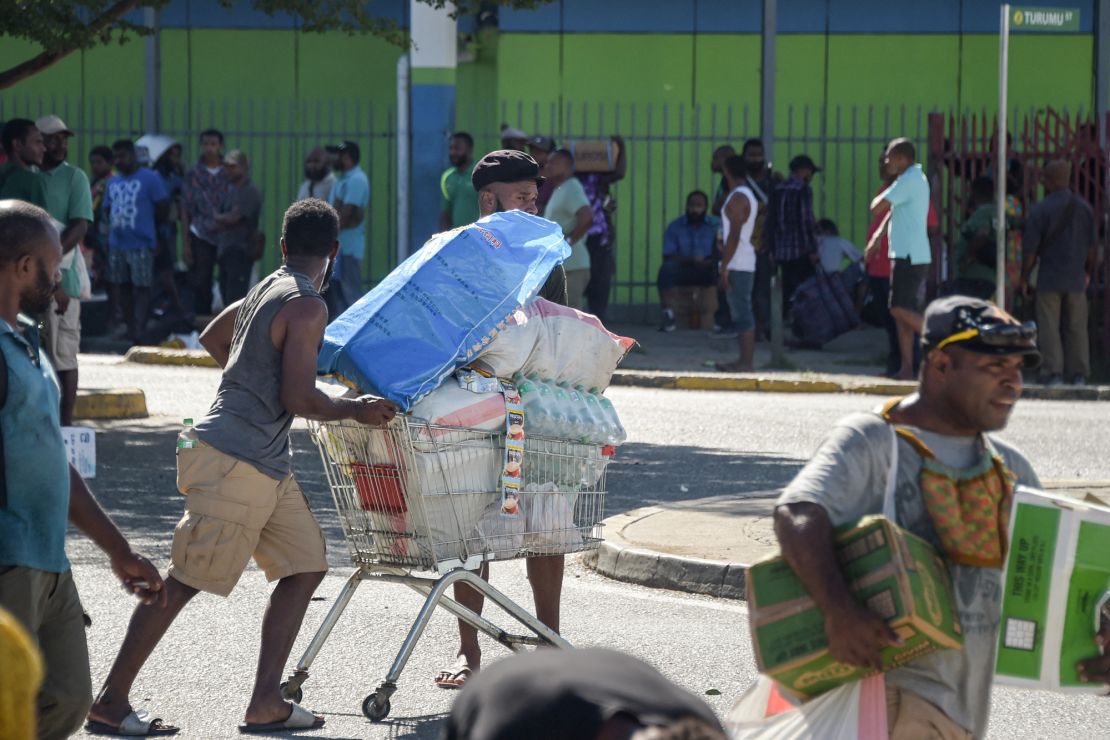 A man pushes a shopping trolley on the street as crowds leave shops with looted goods amid a state of unrest in Port Moresby on January 10, 2024. A festering pay dispute involving Papua New Guinea's security forces on January 10 sparked angry protests in the capital, where a crowd torched a police car outside the prime minister's office. By Wednesday afternoon pockets of unrest had spread through the capital Port Moresby, with video clips on social media showing crowds looting shops and stretched police scrambling to restore order. (Photo by Andrew KUTAN / AFP) (Photo by ANDREW KUTAN/AFP via Getty Images)
