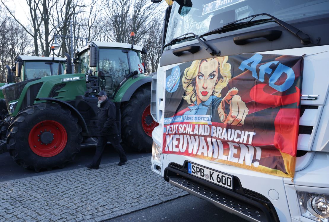 BERLIN, GERMANY - JANUARY 08: A man walks past the tractors of protesting farmers and a banner with the logos of the far-right Alternative for Germany (AfD) political party that reads: "Germany Needs New Elections!" on the first day of a week of protests on January 08, 2024 in Berlin, Germany. Farmers are protesting across Germany this week against proposed government measures that would reduce federal benefits for the agricultural sector. While the coalition government recently stepped back from some of the measures, including a proposed taxation of agricultural vehicles and cutting agricultural fuel subsidies, farmers have vowed to press on with their protests in order to stop any measures from being enacted at all. The government is seeking to save EUR 100 million in its agriculture budget. (Photo by Sean Gallup/Getty Images)