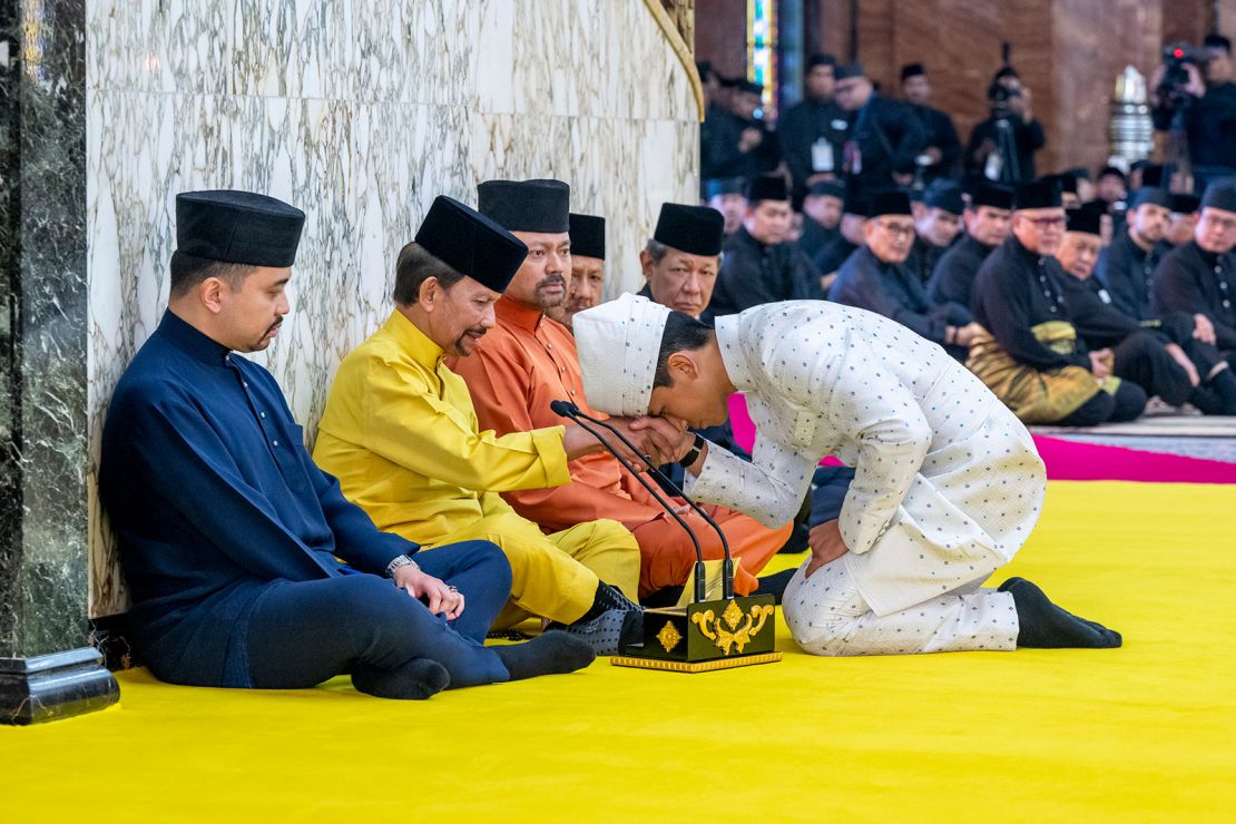 This handout picture taken by Brunei's Information Department on January 11, 2024 and released on January 12, 2024 shows Brunei's Prince Abdul Mateen, right, touching his forehead on his father's hand, Brunei's Sultan Haji Hassanal Bolkiah, second from left, after his solemnization at Sultan Omar Ali Saifuddien Mosque in Bandar Seri Begawan, Brunei.