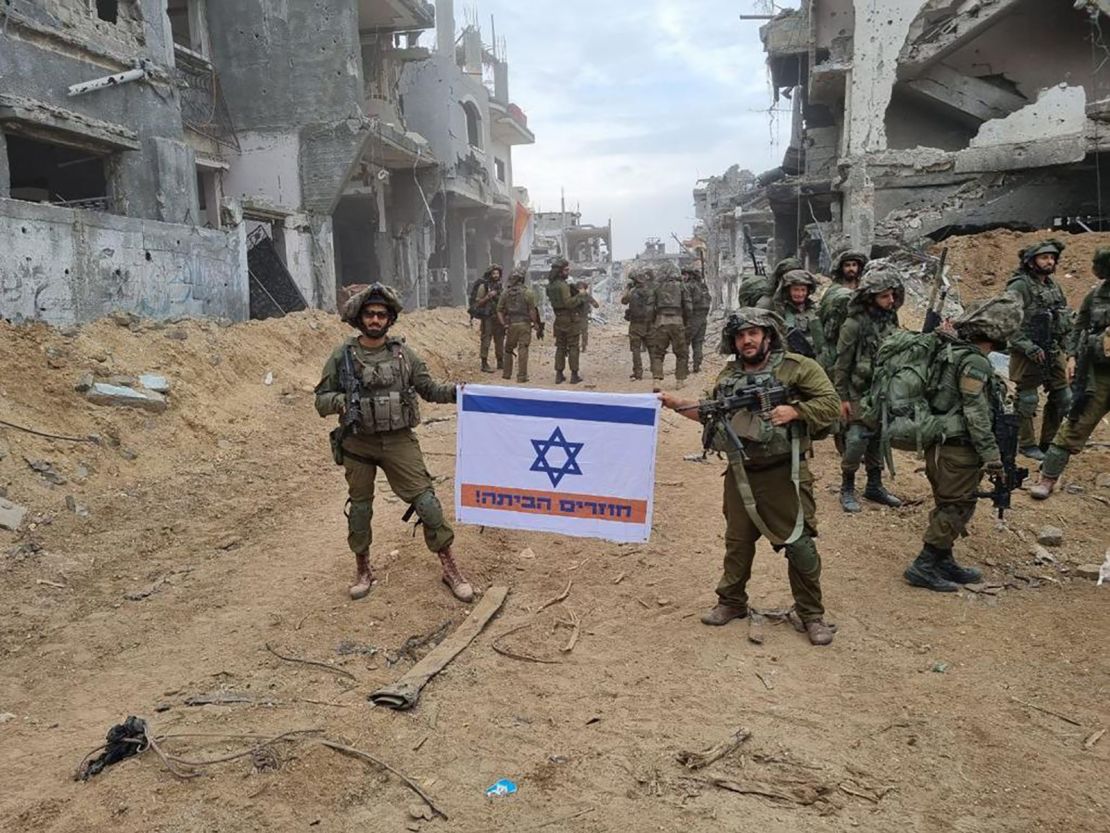Two soldiers in Gaza hold an Israeli flag, altered to include an orange stripe and the words, in Hebrew: “Coming home!”
