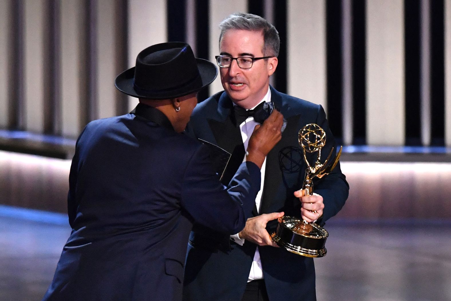 Arsenio Hall adjusts John Oliver's bowtie on stage after "Last Week Tonight with John Oliver" won another Emmy. Oliver collected awards for outstanding scripted variety series and outstanding writing for a variety series.