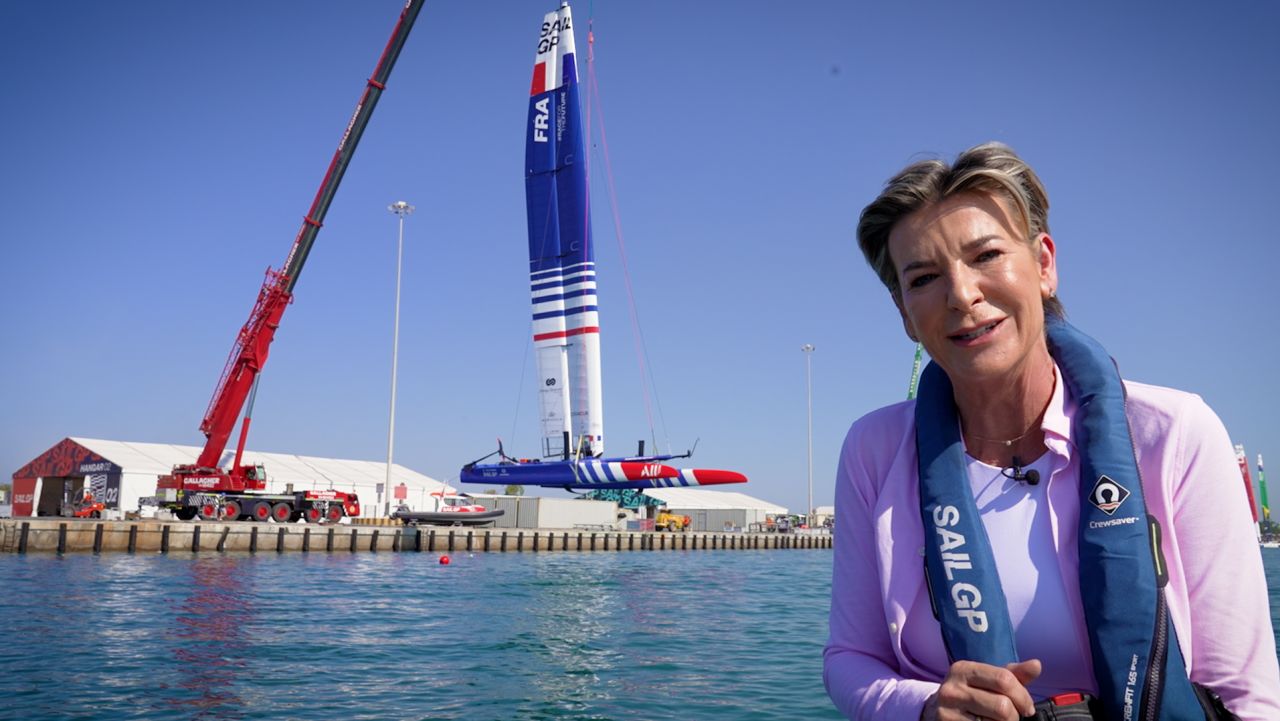 CNN's Becky Anderson at the Abu Dhabi Sail Grand Prix while an F50 catamaran is winched into the water behind her. 