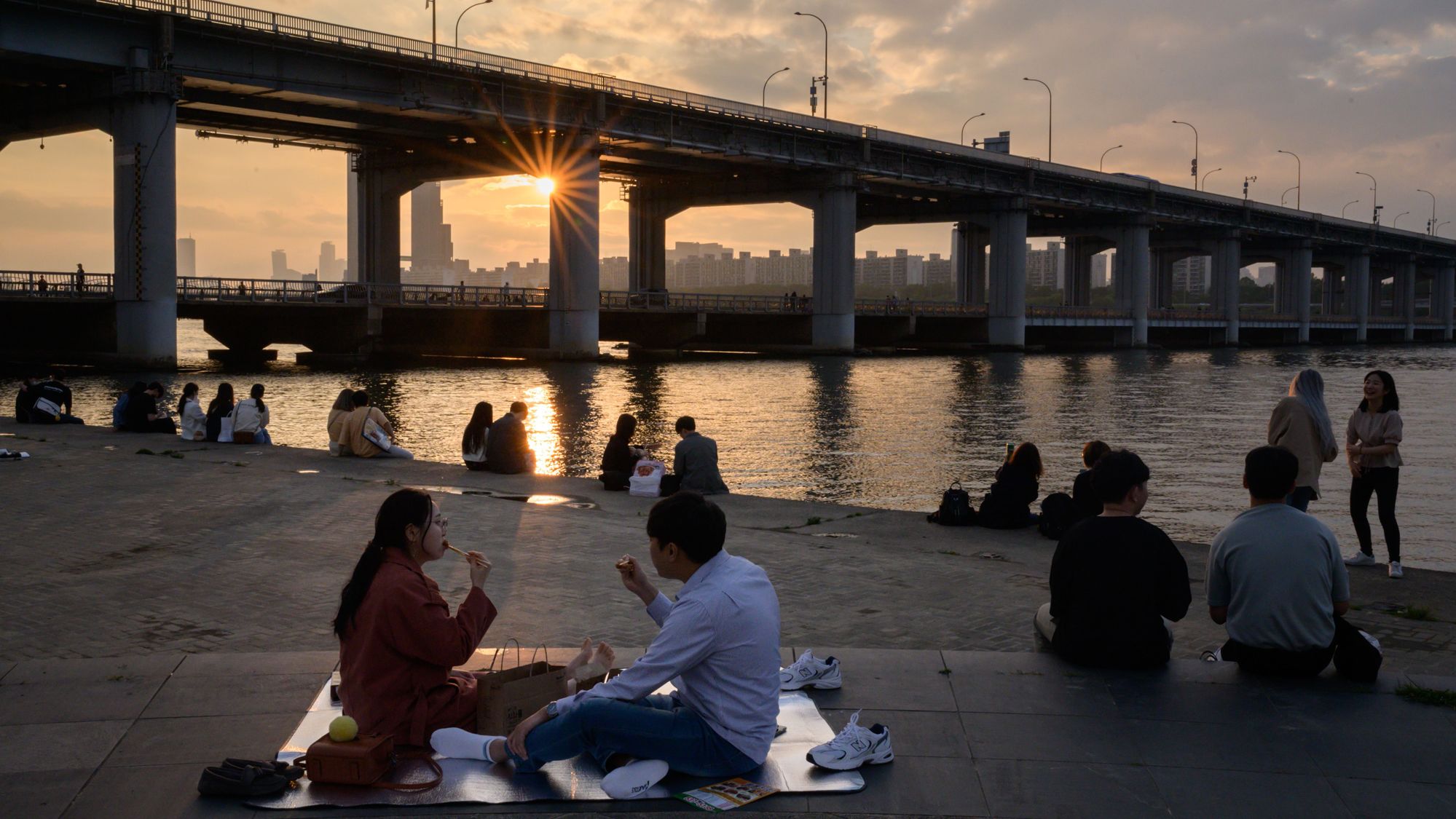 TOPSHOT - In a photo taken on May 24, 2020, people sit before the city skyline and Han river in a park in Seoul. (Photo by Ed JONES / AFP) (Photo by ED JONES/AFP via Getty Images)