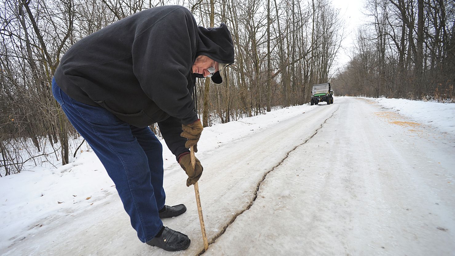 In a Saturday, Jan. 11, 2014 photo, Dennis Olsen measures a giant fissure, which he measured to be an inch wide and at least eight to ten inches deep, in his rural driveway in Waupun, Wis., after a weather phenomenon known as an ice quake occured recently. It results from water freezing and expanding in the soil and bedrock. (AP Photo/The Reporter, Aileen Andrews) NO SALES