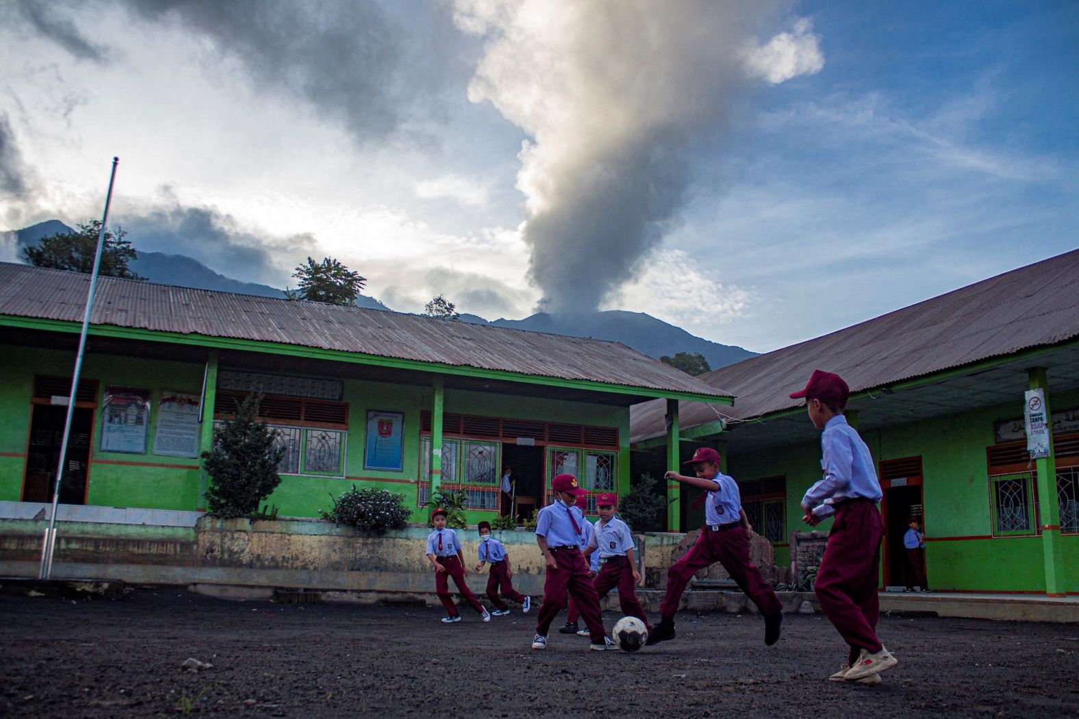 Students play soccer at a school as Mount Marapi spews hot smoke in the distance in Agam, West Sumatra, on Monday, January 15. The volcano's eruption Sunday was its <a href="index.php?page=&url=https%3A%2F%2Fwww.cnn.com%2F2024%2F01%2F14%2Fasia%2Findonesia-volcano-erupts-mount-marapi-intl%2Findex.html" target="_blank">second eruption in weeks</a>.