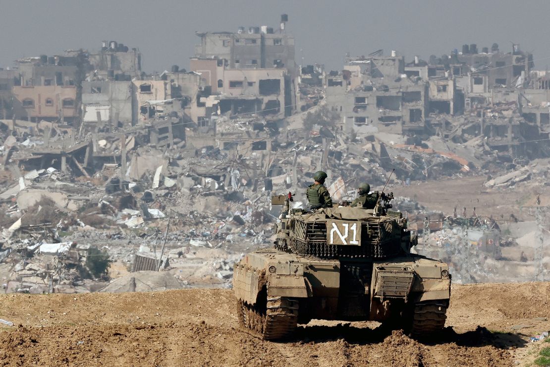 TOPSHOT - A picture taken from a position in southern Israel along the border with the Gaza Strip on January 19, 2024, shows an Israeli tank rolling along the fence as damaged buildings are see in the Gaza strip amid continuing battles between Israel and the militant group Hamas. (Photo by JACK GUEZ / AFP) (Photo by JACK GUEZ/AFP via Getty Images)