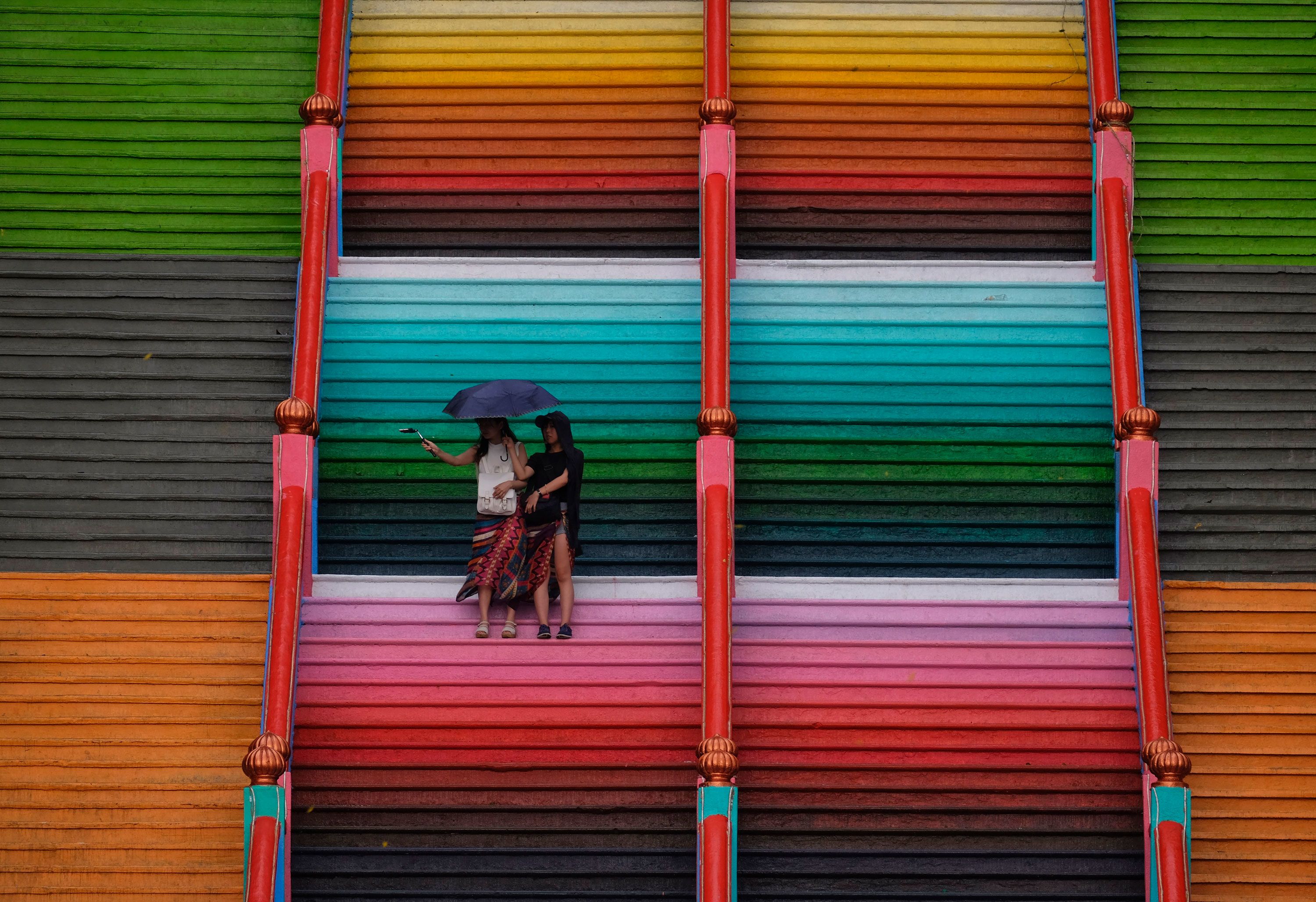 BATU CAVES, MALAYSIA - SEPTEMBER 1: Brightly painted visitors take photos on the 272-step staircase leading to the Sri Subramanian Swamy Temple in Batu Caves, Malaysia on September 1, 2018.  The Sri Subramaniar Swamy Temple has been painted like a rainbow and the temple has been given a colorful new look, a rejuvenation process that is done once in 12 years and is part of the Hindu rituals for its devotees.  (Photo by Mohammad Samsul Mohammad Said/Getty Images)