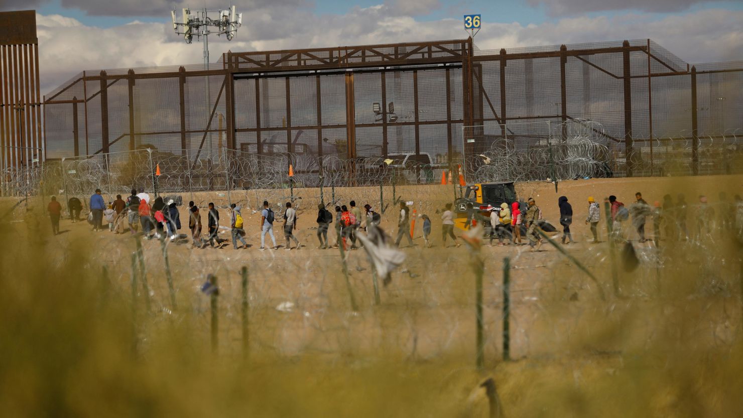 Migrants seeking asylum in the United States gather near the border wall after crossing a razor wire fence deployed to inhibit their crossing into the United States, while members of the Texas National Guard stand guard, as seen from Ciudad Juarez, Mexico January 22, 2024.